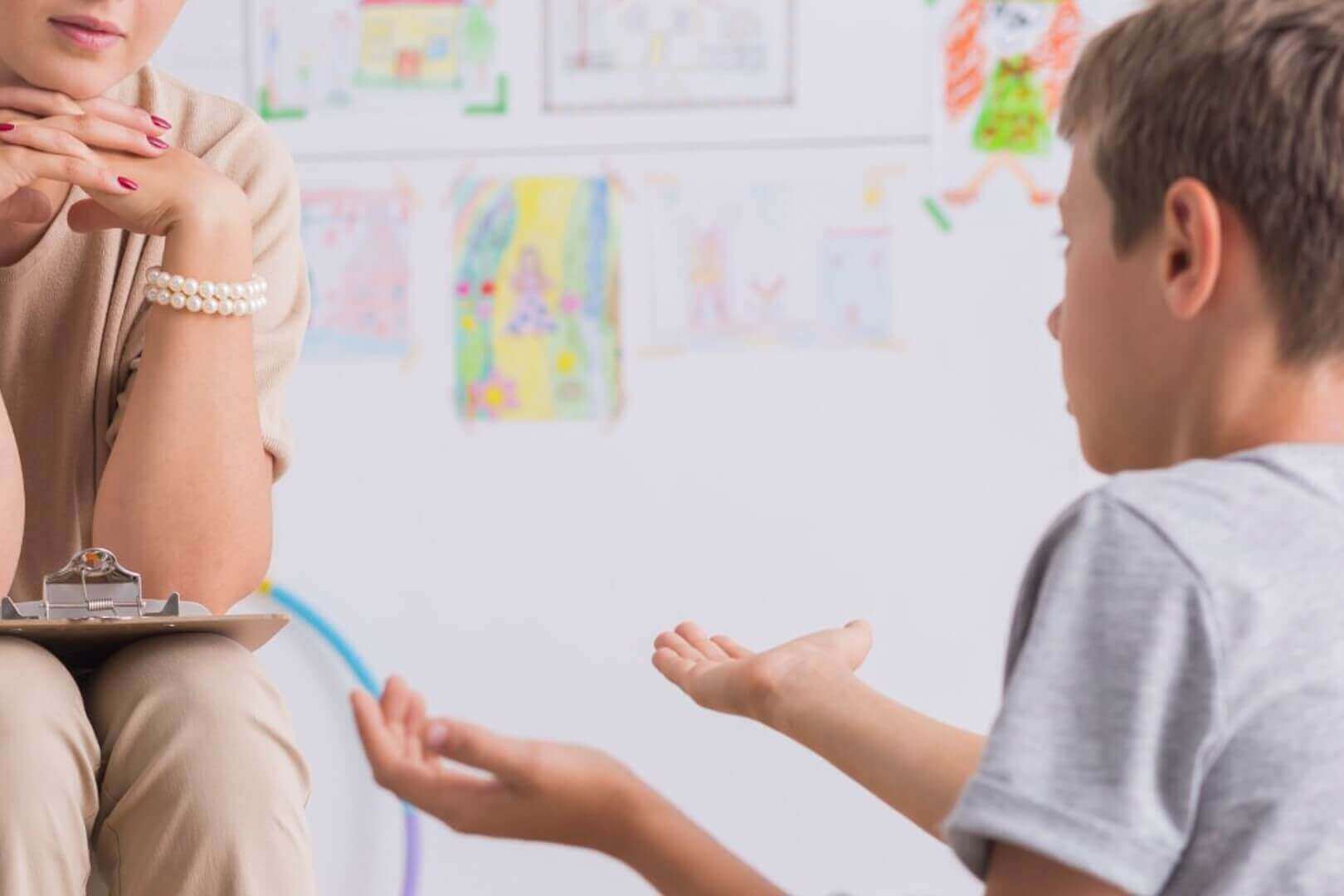 Child in therapy session with counselor, expressive hands, colorful drawings on wall, emotional support, child counseling.