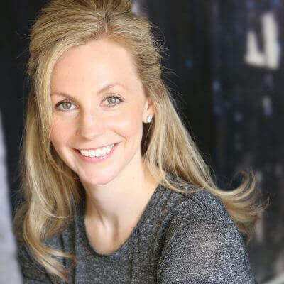 Smiling woman with blonde hair in a gray sweater, studio background, professional portrait photography.