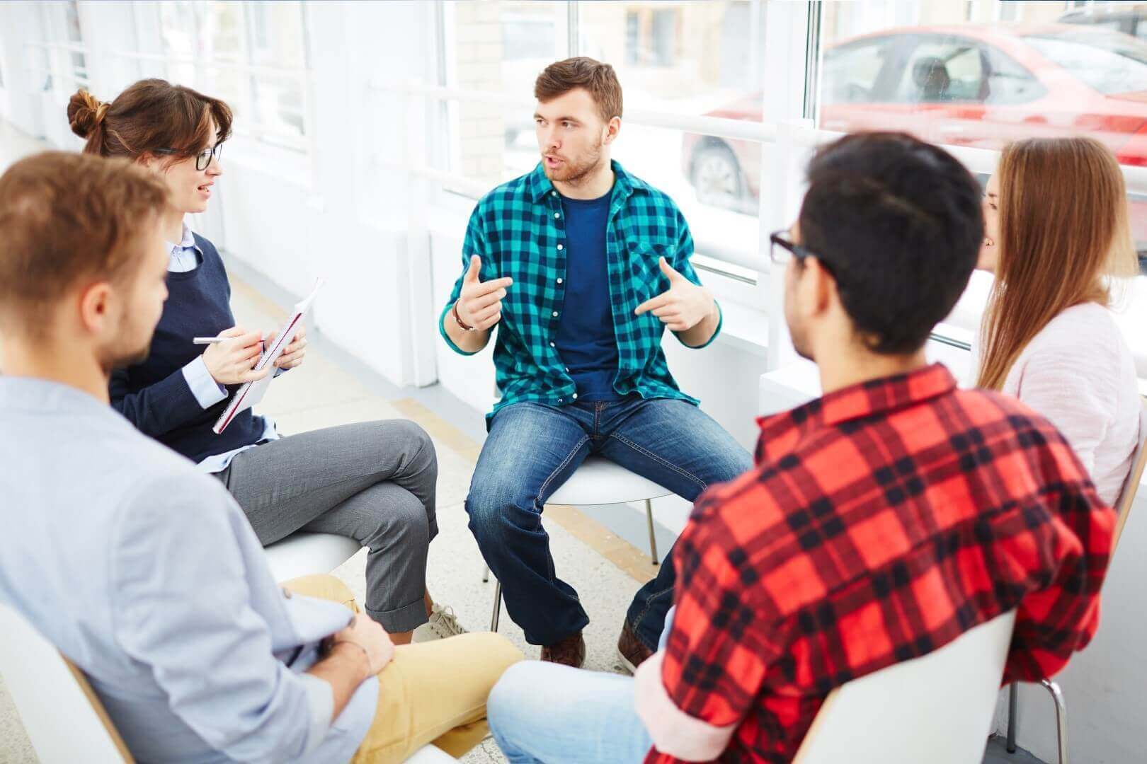 Group counseling session with diverse participants discussing and sharing in a bright, modern room.